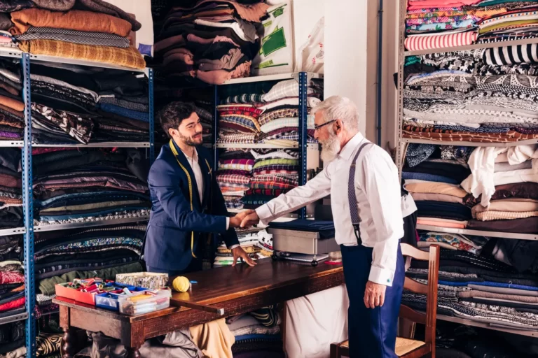 senior-male-customer-shaking-hands-with-young-male-tailor-his-workshop